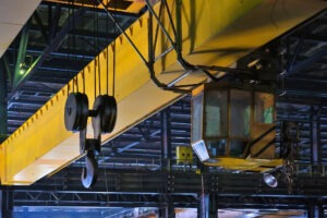 Industrial overhead crane with a hook and pulley system, suspended in a warehouse, highlighting machinery used for heavy lifting.